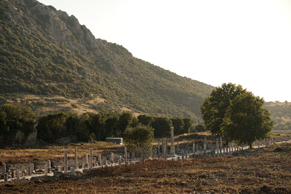 Explore serene ancient ruins set against a majestic mountain backdrop bathed in soft sunlight.