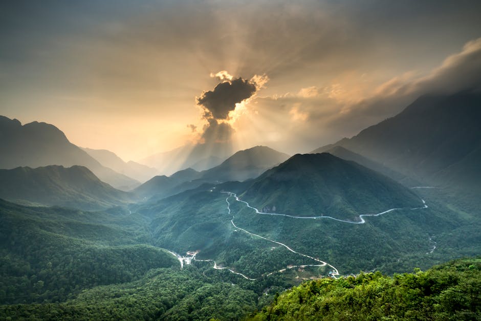 Stunning landscape of a sunlit mountain range with winding roads and dense forests at sunset.